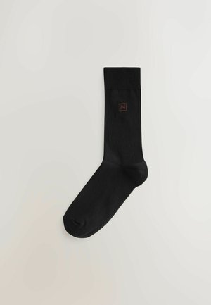 Șosetă din bumbac negru, cu manșetă ribbată, având un logo discret în partea superioară. Textură netedă și design ajustat pentru confort.