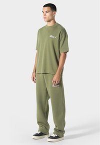 Vihreäoliivinvärinen ylipitkä t-paita ja siihen sopivat collegehousut, jotka on valmistettu pehmeästä kankaasta, jossa on sileä pinta ja hillitty brändäys rinnassa ja reidessä.