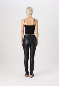 Canotta nera aderente con spalline sottili abbinata a pantaloni in ecopelle nera, caratterizzati da una texture liscia e una finitura leggermente lucida.