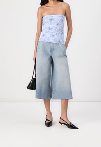 Top bez ramiączek w kwiaty w jasnoniebieskim kolorze, zestawiony z szerokimi, jasnoniebieskimi dżinsami i czarnymi sandałkami na obcasie. Mała czarna torebka trzymana w ręku.