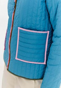 Quiltowana niebieska kurtka z kieszenią wykończoną różowym brzegiem, kontrastowym zamkiem błyskawicznym i teksturowanym materiałem. Slim fit z widocznymi detalami szycia.