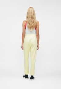 Gaiši dzelteni sporta bikses ar brīvu piegriezumu, elastīgu jostasvītu un potīšu aprocēm, savienotas ar pelēku bezpiedurkņu topu ar sarkanām siksnām.