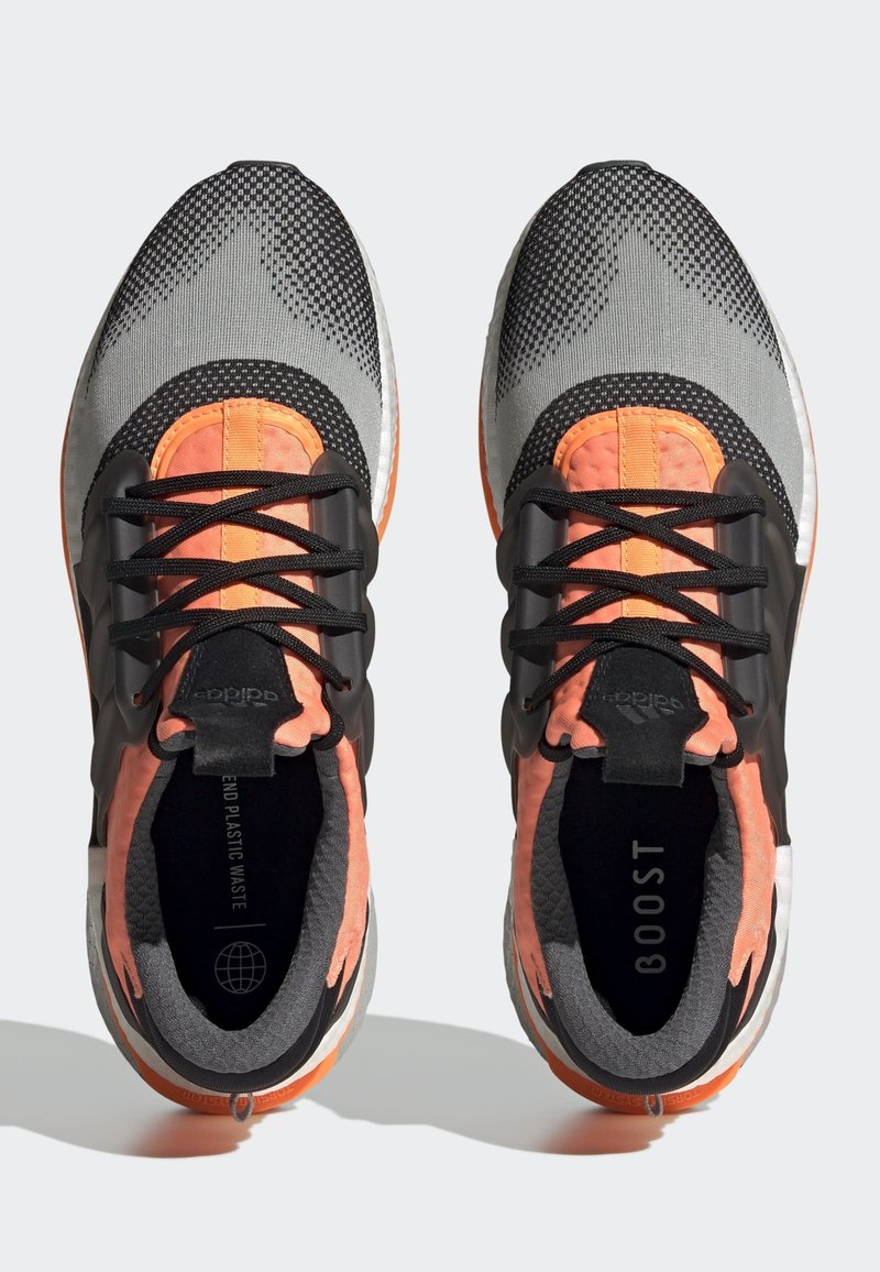 Zapatillas deportivas en gris con acentos en negro y naranja; parte superior de malla, lengüetas acolchadas, cordones negros, suelas acolchadas y detalles texturizados.