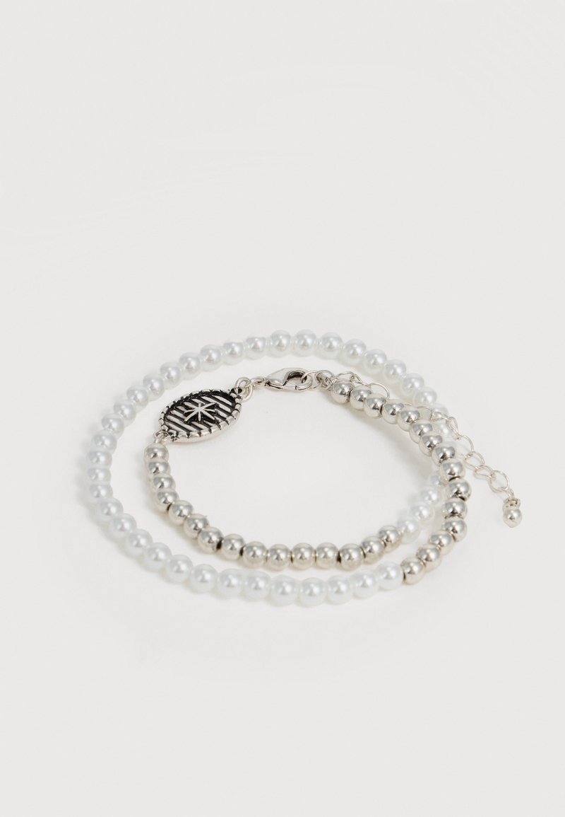 Bracelet double rangée avec perles blanches alternées et perles argentées, avec un pendentif ovale en argent orné d'un motif étoile et une fermeture mousqueton.