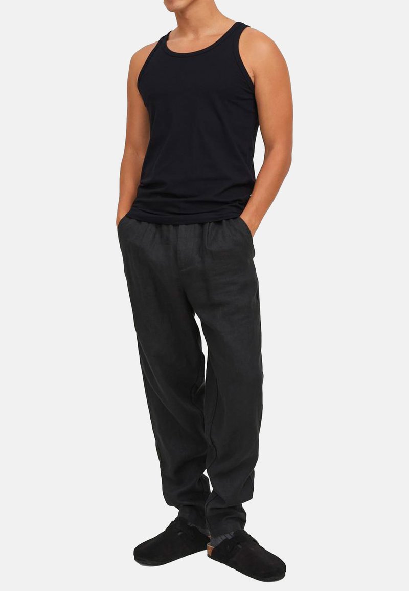 Débardeur noir en coton, pantalon en lin gris décontracté et chaussures noires. La tenue présente un design simple avec une taille élastique.