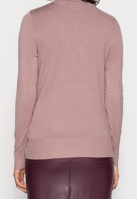 Cardigan di un morbido rosa con maniche lunghe, orlo a coste e texture liscia. Presenta un design semplice; senza pattern visibili o dettagli in metallo.