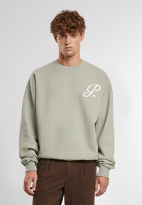 Lys grønn sweatshirt med rund hals og løs passform. Har en liten hvit logo på brystet og ribbestrikkede mansjetter. Myk stofftekstur.