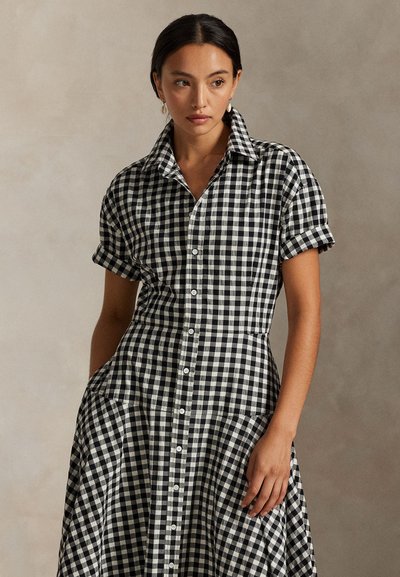 Zwart-wit geruite blousejurk met een getailleerd lijfje, korte mouwen en knoopdetails. Voorzien van een uitlopende rok en kraag.