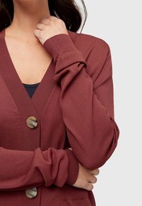 Kardigan v rezavé barvě, s výstřihem do V, se dvěma velkými knoflíky a žebrovanými manžetami. Měkká, texturovaná tkanina s uvolněným střihem.