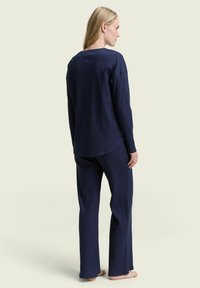 Marineblauw geribbeld loungewear-set met een losvallende lange mouw top en rechte pijpen, die een zachte textuur en een ontspannen ontwerp toont.