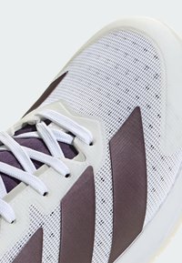 Gros plan sur une basket blanche avec des accents violets, des lacets blancs et un dessus en mesh présentant un motif à grille.
