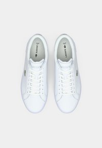 Baskets blanches en cuir avec bout rond, design à lacets et logo crocodile vert sur le côté. Intérieur gris clair avec la marque Ortholite.