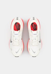 Baskets de course Nike blanches avec des accents rouges, dotées d'une tige en mesh respirant, un amorti visible, des détails de logo noirs et des finitions grises.