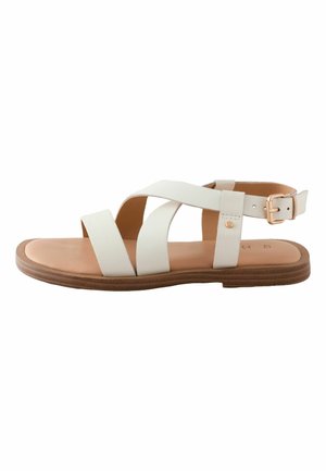 White flat sandal with crossed straps, ankle buckle, tan cushioned footbed, and brown layered sole, designed for casual wear.