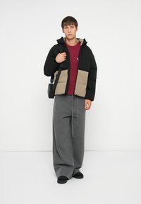 Black and beige puffer jacket with a hood, zip closure, and pockets; paired with a maroon t-shirt and loose gray pants. Black footwear.