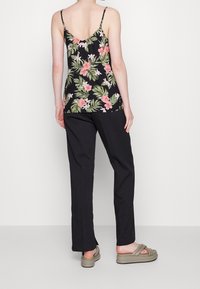 Kwiatowa koszulka na ramiączkach na czarnym tle z różowymi i zielonymi wzorami, zestawiona z czarnymi spodniami i oliwkowymi sandałami.