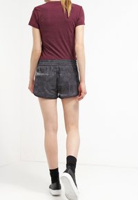 Mörkgrå mönstrade shorts med resårmidja, kombinerat med en vinröd åtsittande t-shirt, bärs med svarta strumpor och vita sneakers.