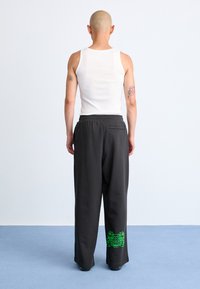 Sorte sweatpants med snoreliv, prydet med et grønt grafisk design på venstre ben. Materialet ser blødt og tekstureret ud.