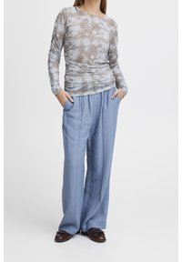 Långärmad topp i ett gråbrunt ormskinnsmönster kombinerad med ljusblå vida byxor. Båda har en jämn yta.