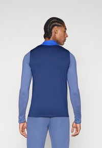 Long-sleeve athletic shirt featuring a color-block design with a navy blue back and light blue sleeves. Soft, stretchy fabric with a collar.