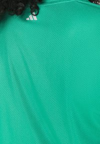 Grön mesh träningsskjorta med rund halsringning, med en liten vit Adidas-logotyp på övre vänstra sidan. Lätt och andningsbart material.