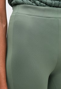 Φαρδύς, εφαρμοστός κολάν με ψηλή μέση σε ήπιο πράσινο ύφασμα με λεία υφή, με λεπτομέρειες στις ραφές για επιπλέον δομή.