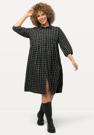 Langärmliges, knöpfbares Kleid im schwarz-grauen Karomuster. Verfügt über eine leicht ausgestellte Form, einen Schlitz vorne und ein strukturiertes Material.