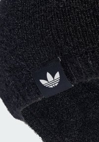 Schwarze gestrickte Mütze mit strukturiertem Stoff, umgeschlagenem Rand und einem rechteckigen Etikett, das ein weißes Trefoil-Logo zeigt.