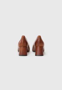 Brown leather high-heeled shoes with a rounded toe and block heel. Smooth texture with minimal stitching on the back.