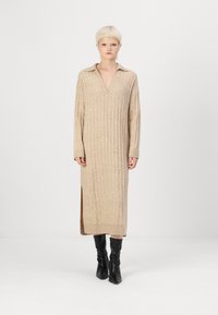 Beige ribbelt kötött ruha V kivágással és gallérral, hosszú ujjú, oldalsó hasítékokkal és laza szabással, fekete térd fölé érő csizmával viselve.