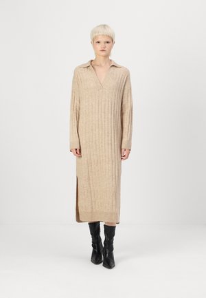 Beige ribbad stickad klänning med V-ringning och krage, långa ärmar, sidoslitsar och en avslappnad passform, bärs med svarta knähöga stövlar.
