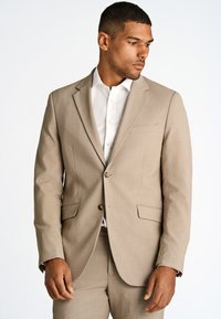 Completo beige chiaro con chiusura a due bottoni, rever a punta e due tasche anteriori. Abbinato a una camicia bianca fresca. Texture liscia.