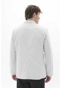 Hellgraue Jacke mit geradem Schnitt, Rückennähten und langen Ärmeln. Hergestellt aus einem glatten, strukturierten Stoff.