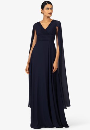 Abito da sera blu navy con scollatura a V, corpino plissettato e maniche a mantello fluttuanti. Il tessuto è morbido, con un design lungo fino al pavimento.