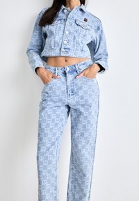 Ljusblå denimjacka i cropped-modell med silverknappar, matchad med byxor som har ett upprepande logomönster, båda i en lös passform.