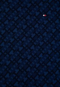 Námořnická modrá tkanina s celoplošným geometrickým vzorem a malou červenou, bílou a modrou obdélníkovou nálepkou v pravém horním rohu.