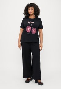 Svart kortermet t-skjorte med motiv av to rosa kirsebær med en sløyfe over og tekst under. Kombinert med vide svarte bukser.