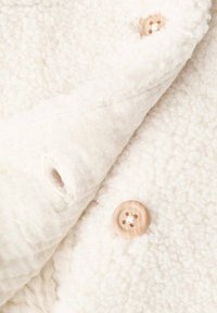 Biele fleece tkanina s textúrovaným, chlpovým povrchom. Obsahuje krémovú ľanovú vrstvu a drevený gombík s štyrmi dierkami.