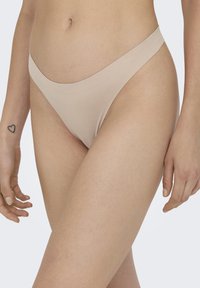 Beige tanga ondergoed van zacht, elastisch materiaal, met een gladde tailleband en een minimaal bedekkend ontwerp. Geen zichtbare patronen.
