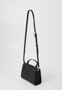 Sac à main noir en matériau texturé, présentant une forme structurée, une anse supérieure et une sangle longue et ajustable avec des accents dorés.