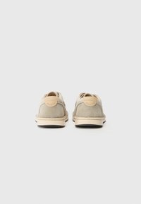 Beige semskede sko med en avrundet form, med en lys farget såle og et sirkulært merkeemblem på hælen.