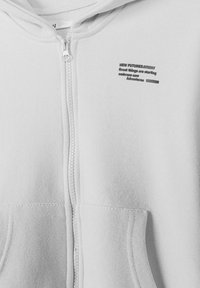 Sweat à capuche blanc avec fermeture éclair, poches avant et texte noir sur la poitrine indiquant "NEW FUTURES De grandes choses commencent, embrassez de nouvelles aventures."