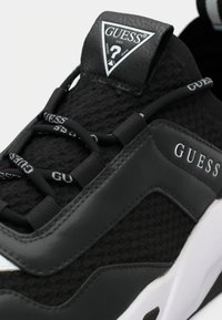 Schwarze Netz- und Synthetikleder-Sneaker mit strukturierter Oberseite, elastischen Schnürsenkeln und einem Logo auf der Zunge. Weiße Sohlelemente.