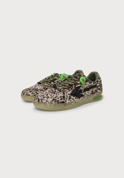 Paire de baskets basses avec motif marron et blanc tacheté, lacets verts, motif flèche noire et semelles beiges translucides sur fond blanc.