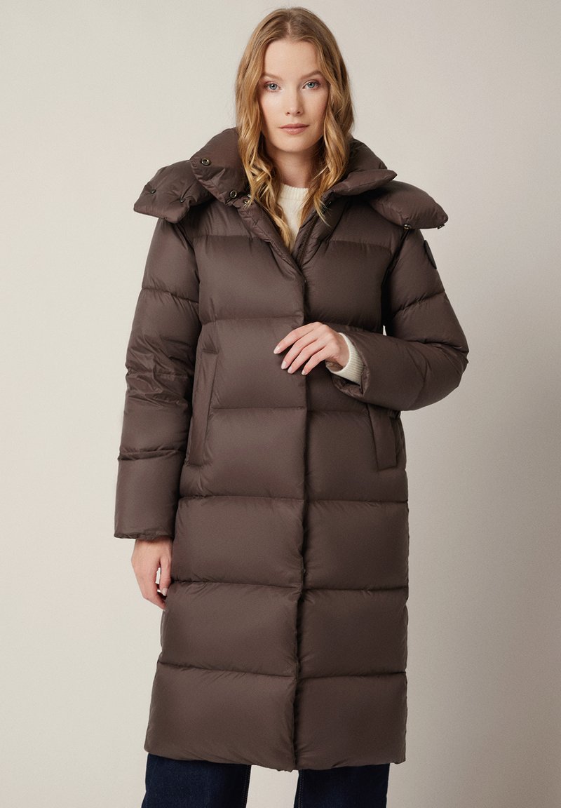 Brązowa kurtka puchowa o teksturowanym, pikowanym wzorze, z dużym kołnierzem i guzikami. Posiada kieszenie boczne i długość do kolan.