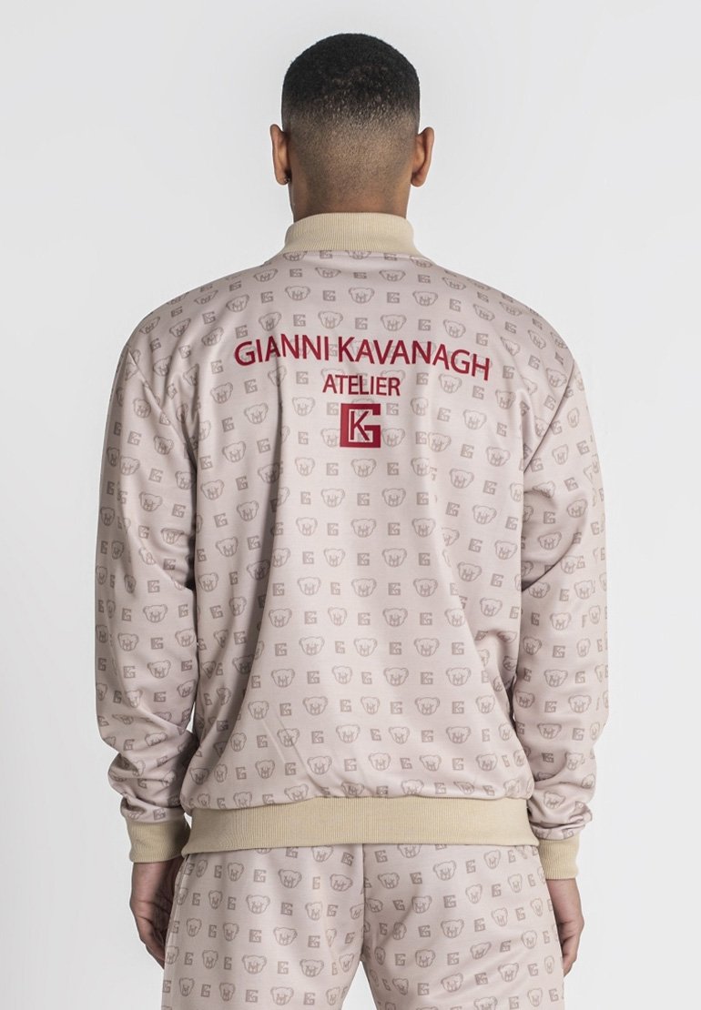 Lichtbeige jasje met herhalend logo-patroon, geribde manchetten en zoom, en rood geborduurde tekst "GIANNI KAVANAGH ATELIER" op de achterkant.