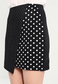 Černá minisukně s kombinací malých a velkých bílých puntíků z texturované látky. Obsahuje design ve stylu zabalování.