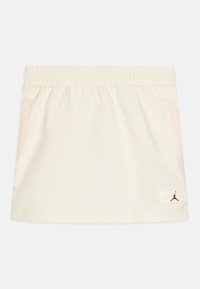 Skort de color crema con cinturilla elástica, dos bolsillos laterales y acentos rosas. Presenta un pequeño logo rojo de Jordan cerca del dobladillo.