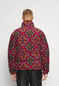 Maroon puffer jacket with an intricate multicolor floral pattern. High collar, elastic cuffs, and a slightly loose fit for comfort.