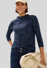 Maglietta a maniche lunghe blu navy con motivo a strisce di tigre, scollo rotondo e forma attillata, abbinata a jeans scuri e una borsa color crema.